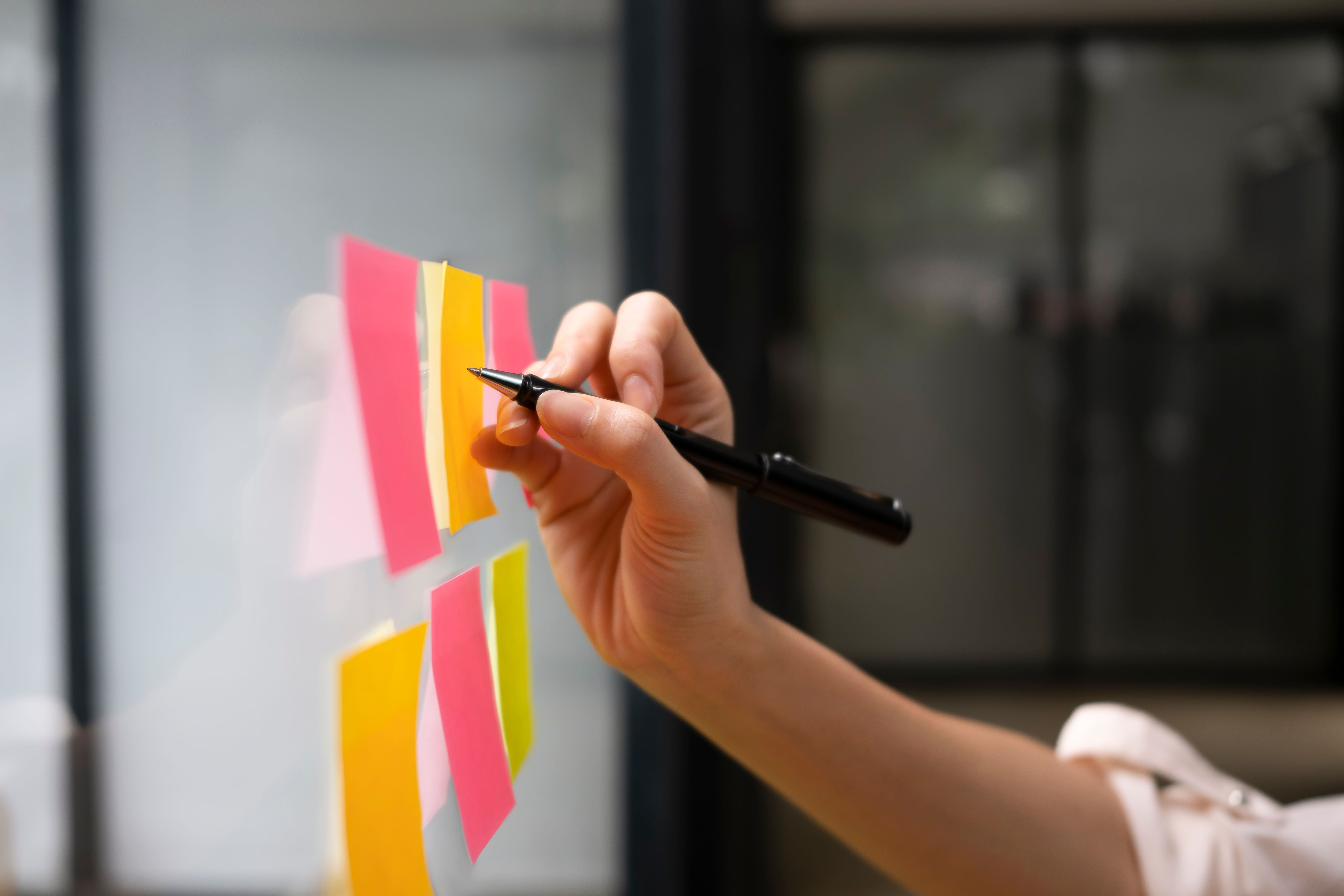 Hand shown writing on sticky notes that are stuck on a glass wall. 